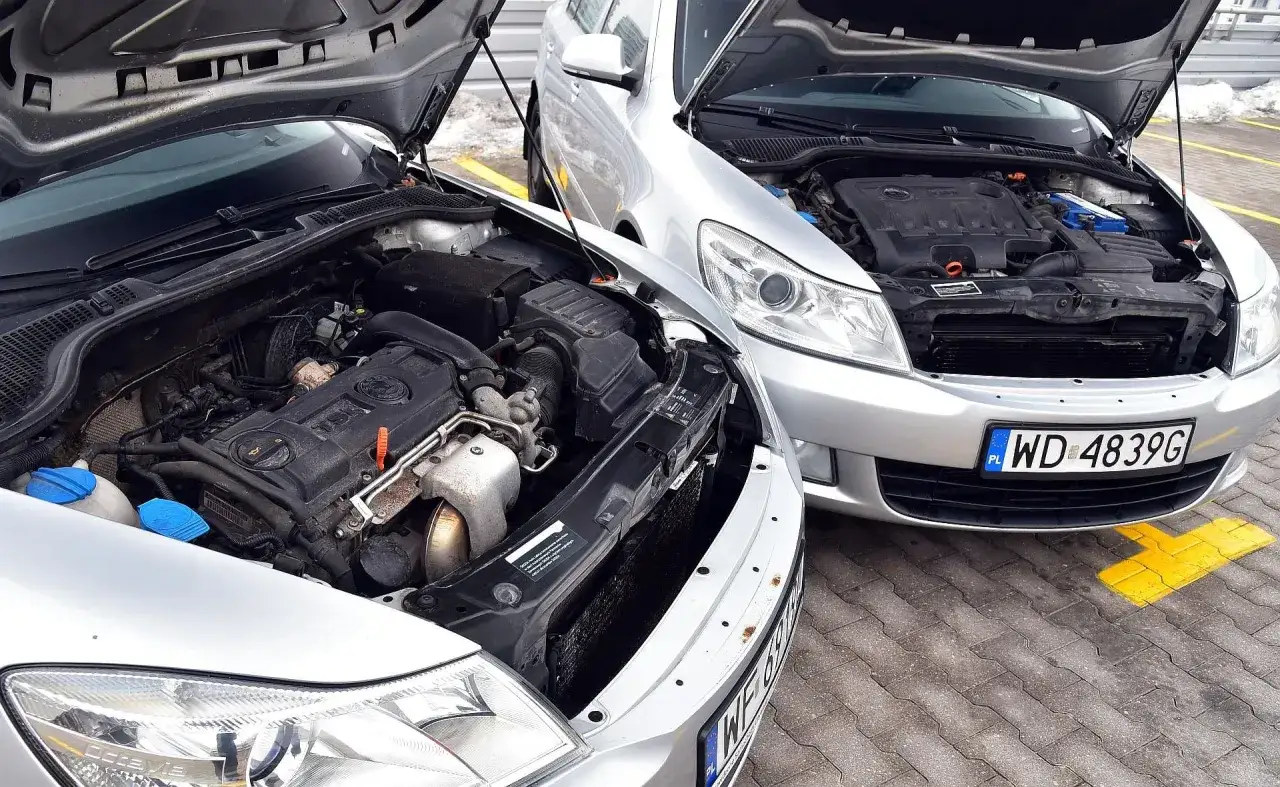 Dwa srebrne samochody z otwartymi maskami. Silnik wysokoprężny to diesel, a nie benzyna, co widać po budowie jednostki napędowej.