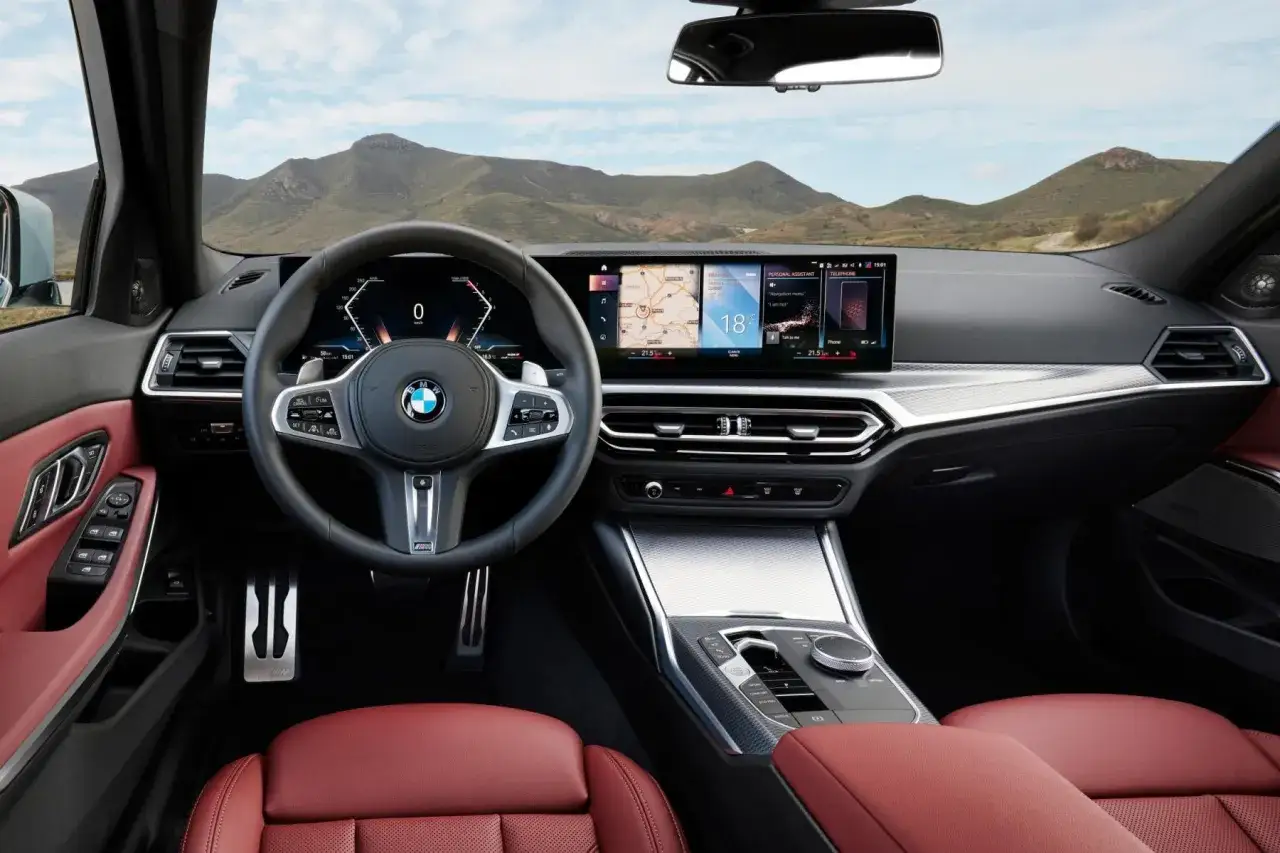 Wnętrze BMW 318i z czerwonymi skórzanymi fotelami, nowoczesnym panelem cyfrowym i nawigacją.