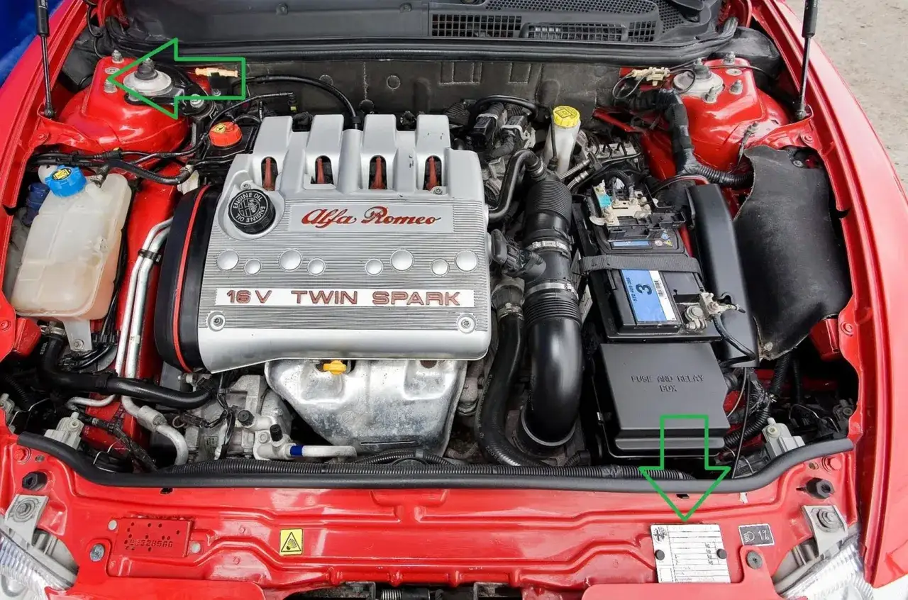 Silnik Alfa Romeo 147 1.9 JTD z widocznym osprzętem, akumulatorem i skrzynką bezpieczników. Zielone znaczniki wskazują elementy.