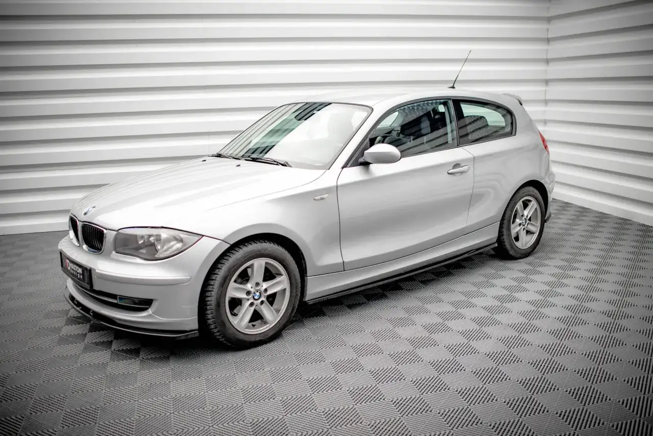 Srebrne BMW e81, kompaktowe i sportowe, prezentuje się elegancko na tle nowoczesnej, białej ściany.