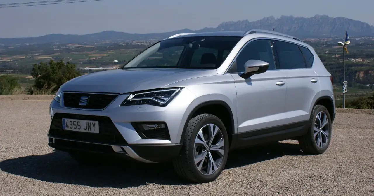 Srebrny Seat Ateca zaparkowany na żwirowej drodze z widokiem na górzysty krajobraz.