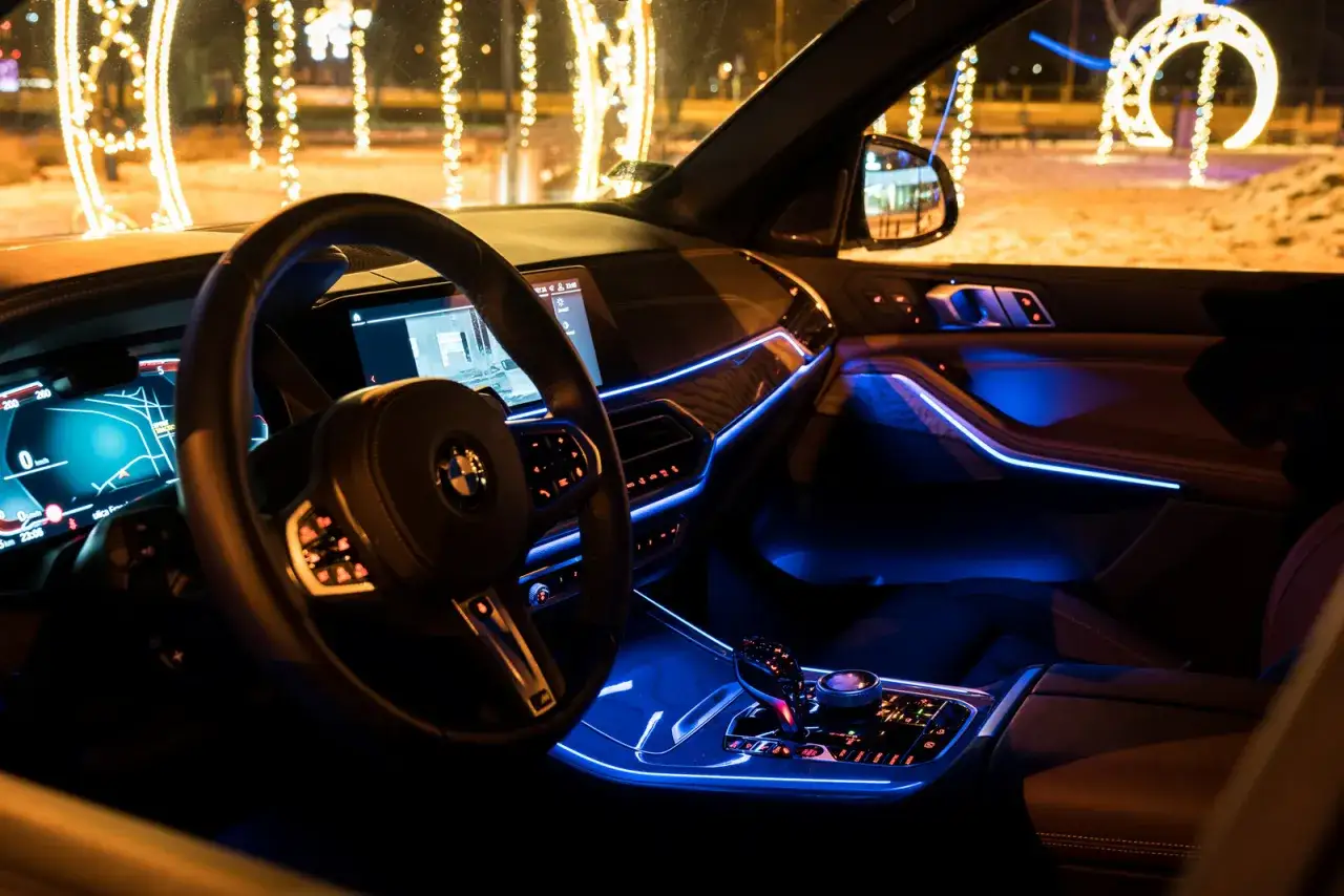 Wnętrze BMW G05 nocą, z niebieskim nastrojowym oświetleniem i świątecznymi iluminacjami na zewnątrz.