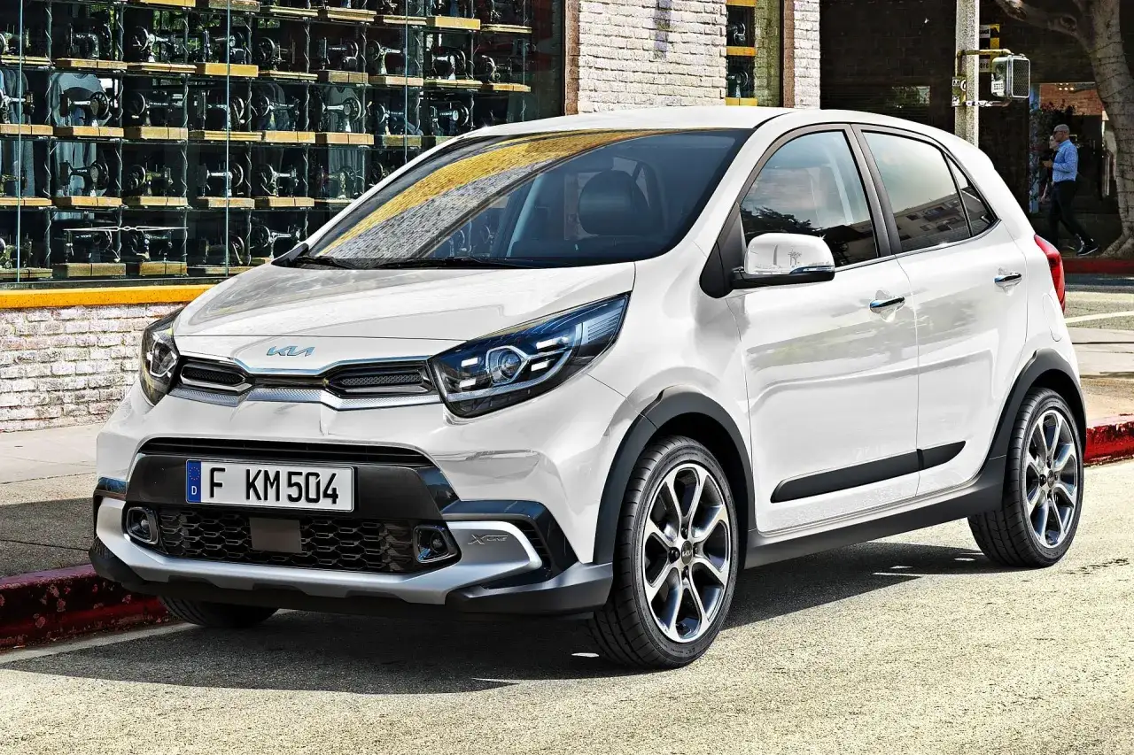 Biały Kia Picanto X-Line, jeden z popularnych kia modele, parkuje na ulicy przed budynkiem z wystawą maszyn do szycia.