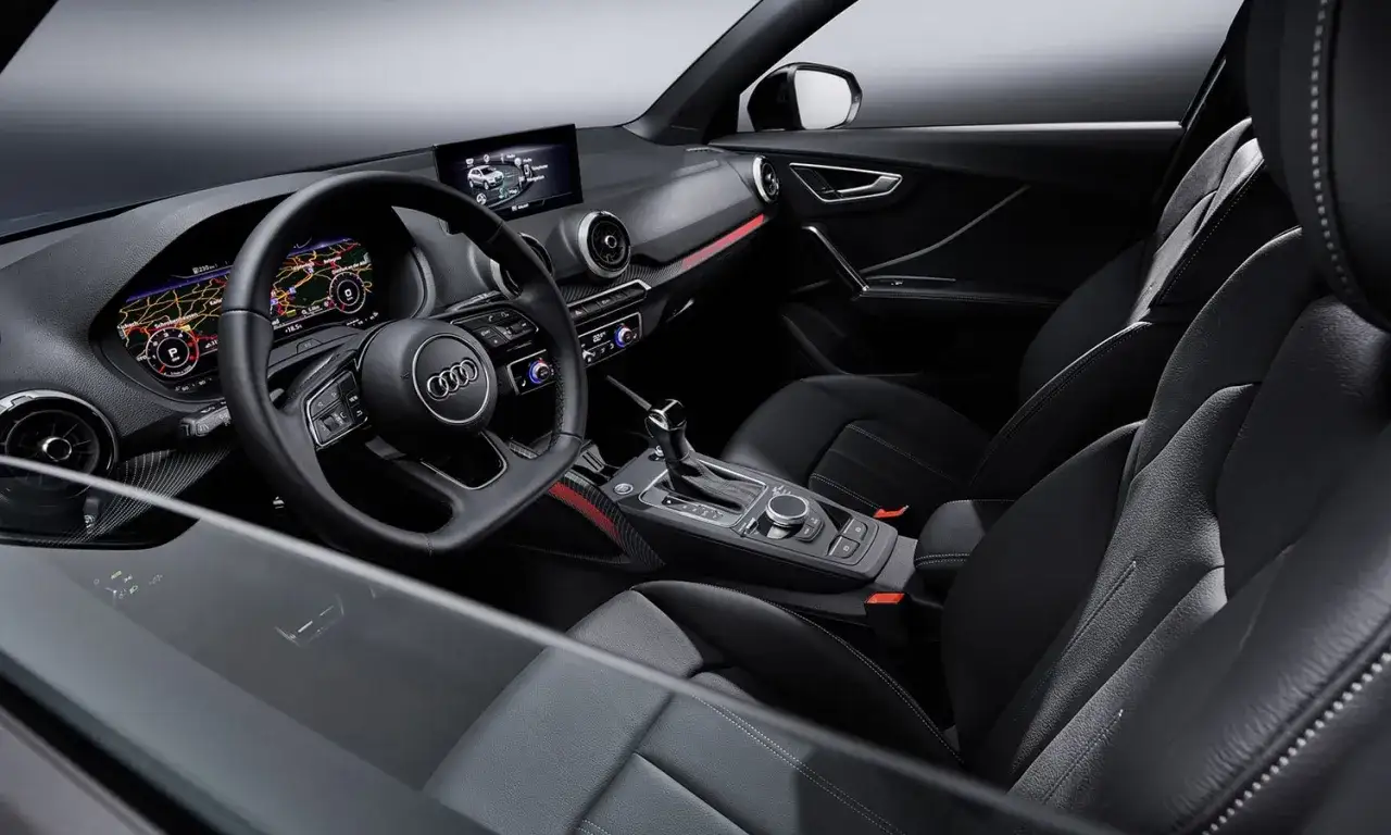 Wnętrze Audi q2: cyfrowe zegary, kierownica, ekran multimediów, czarne fotele i konsola środkowa.