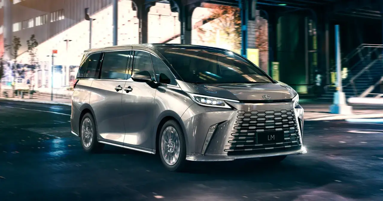 Srebrny Lexus LM 350h sunie nocą przez miasto, oświetlony neonami.