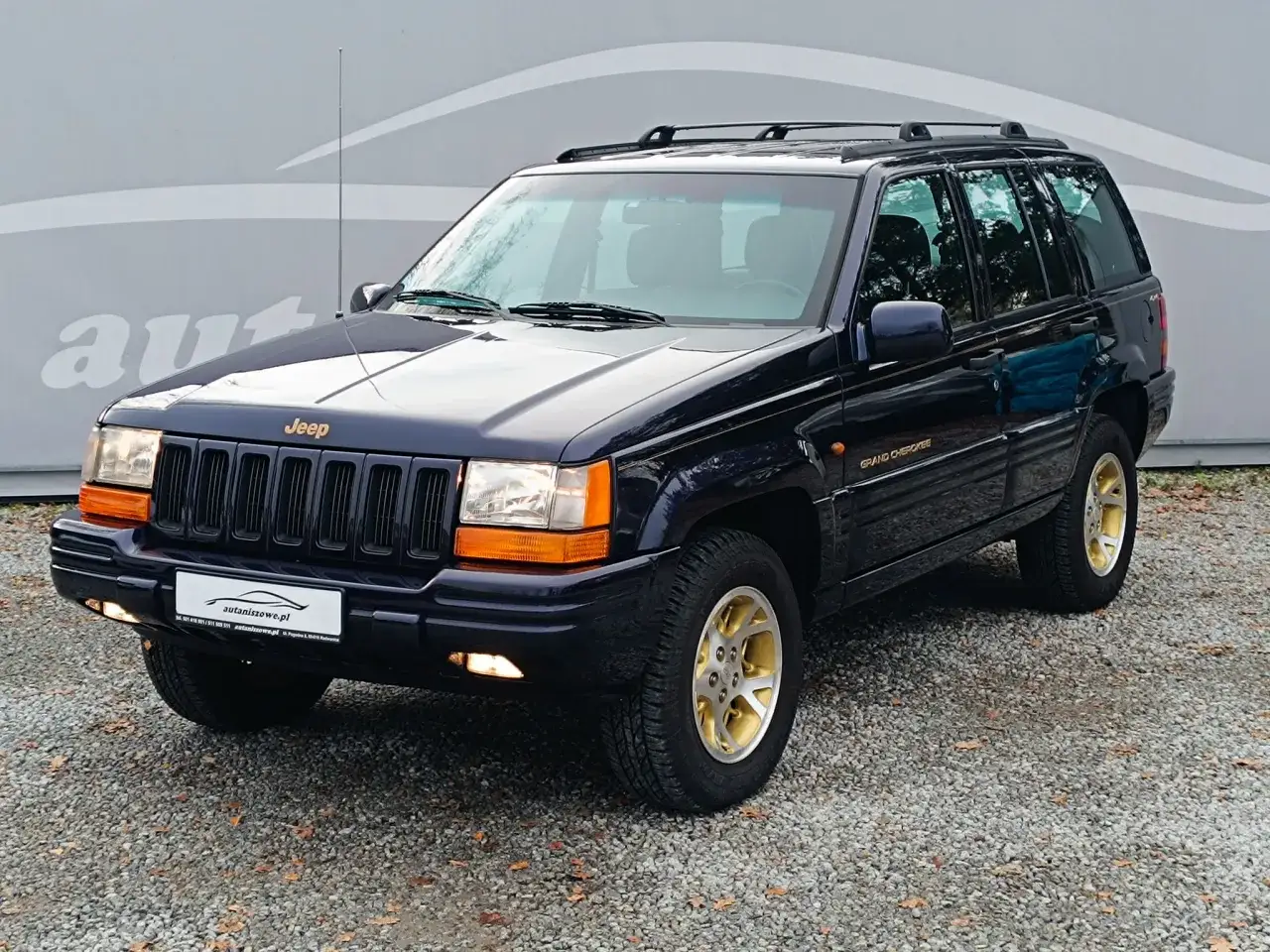Ciemnoniebieski Jeep Grand Cherokee ZJ z lat 90. na złotych felgach, gotowy na przygodę.