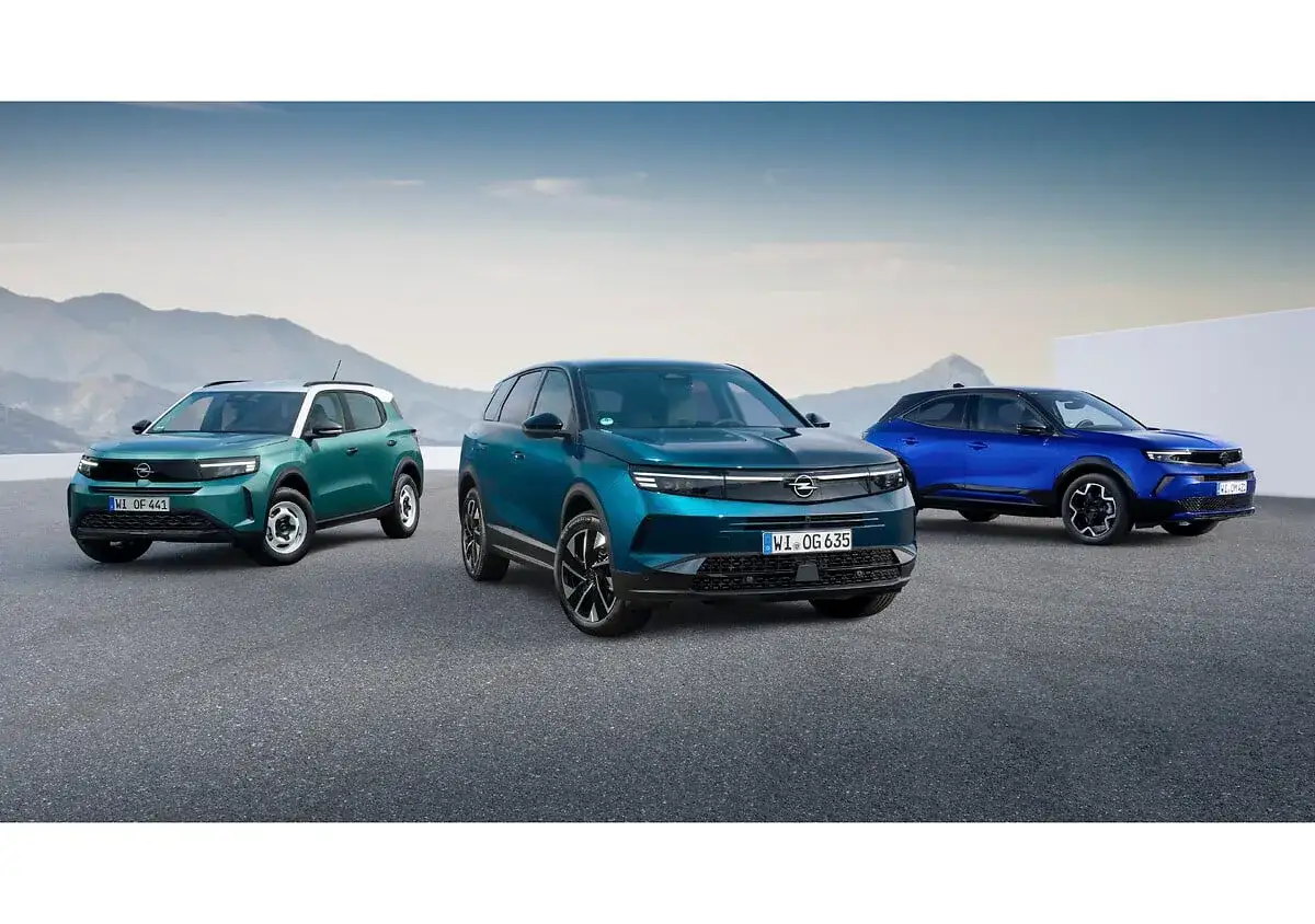 Trzy nowoczesne modele Opla: zielony, ciemnoniebieski i niebieski SUV-y, prezentują się na tle górskiego krajobrazu.
