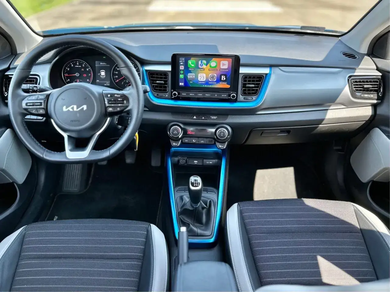 Wnętrze Kia Stonic 2024: kierownica, ekran multimedialny z Apple CarPlay, niebieskie akcenty i wygodne fotele.