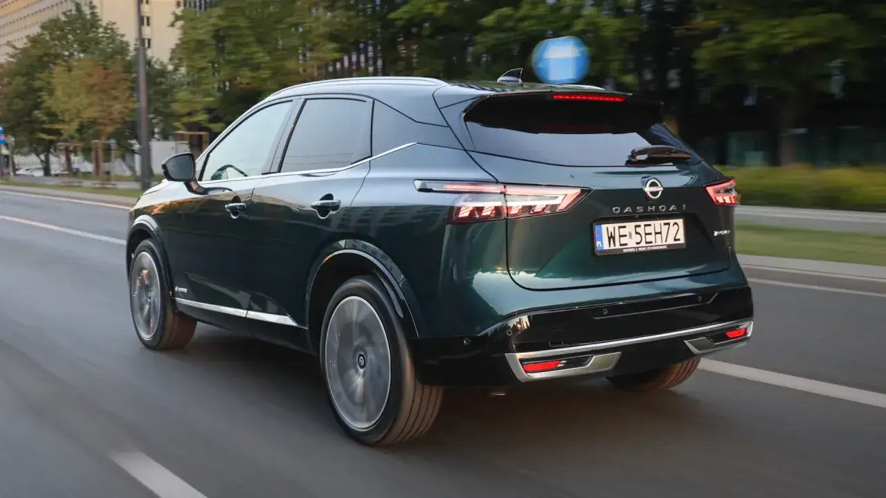 Ciemnozielony Nissan Qashqai, jeden z popularnych nissan modele, jedzie po miejskiej drodze.