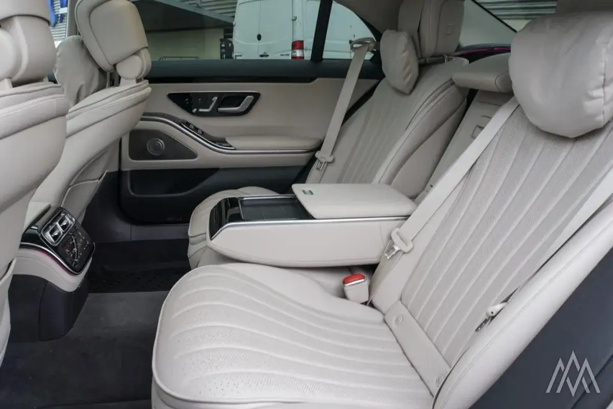 Wnętrze luksusowego mercedesa s400d z jasną, skórzaną tapicerką. Widok na tylne siedzenia, podłokietnik i panele drzwi.