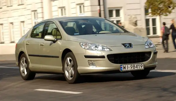Złoty Peugeot 407 2.0 HDI jedzie ulicą.