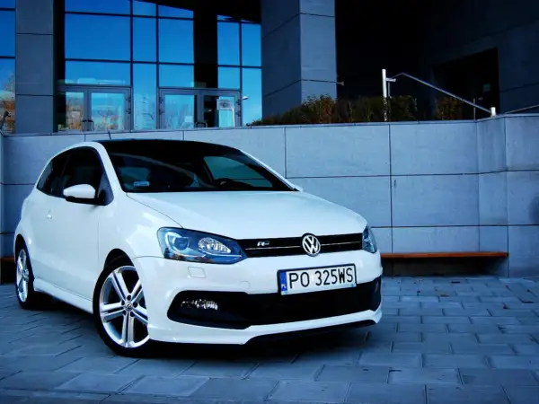 Biały VW Polo 1.2 benzyna z czarnym dachem, zaparkowany przed nowoczesnym budynkiem.