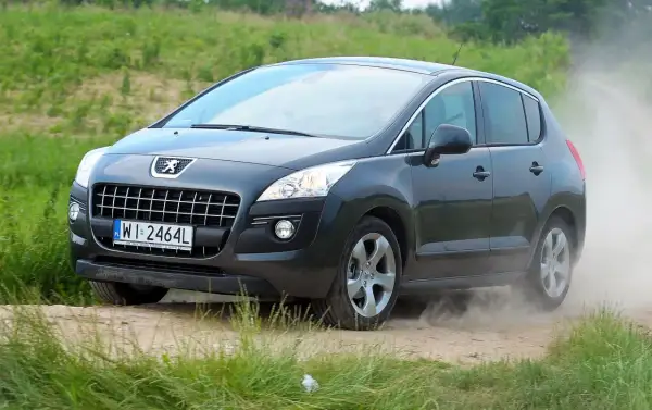 Ciemnoszary Peugeot 3008 1.6 HDI na drodze gruntowej, wzbijający tumany kurzu.