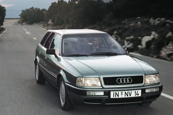 Mężczyzna w garniturze jedzie zielonym Audi 1.9 TDI po krętej drodze.