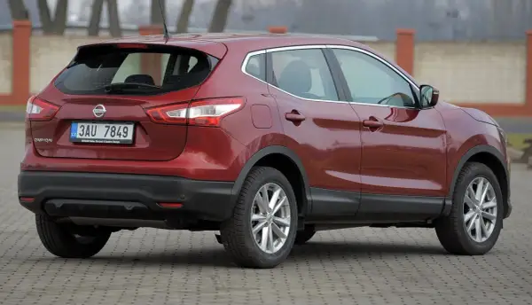 Czerwony Nissan Qashqai 1.6 benzyna z czeskimi tablicami rejestracyjnymi stoi na utwardzonym podjeździe.