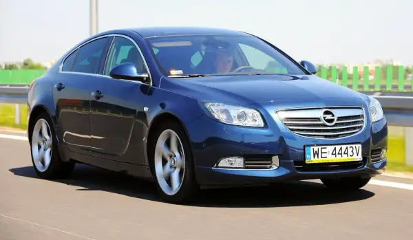 Niebieski Opel Insignia 2.0 Turbo pędzi po drodze, kierowca skupiony na trasie.
