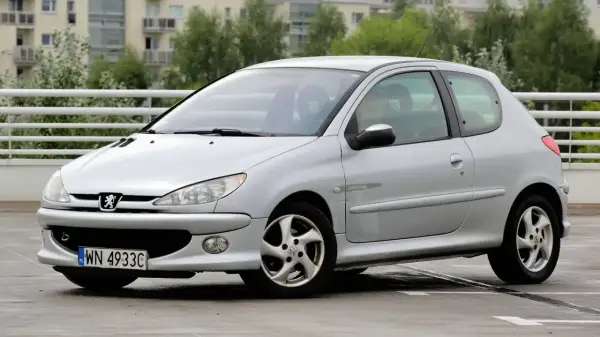 Srebrny Peugeot 206 1.4 benzyna na parkingu. Auto ma sportowy wygląd i jest w dobrym stanie.