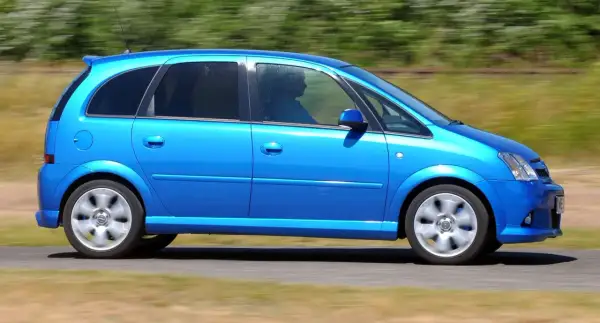 Błękitny Opel Meriva 1.4 benzyna w ruchu, z widocznym kierowcą za przyciemnianą szybą.